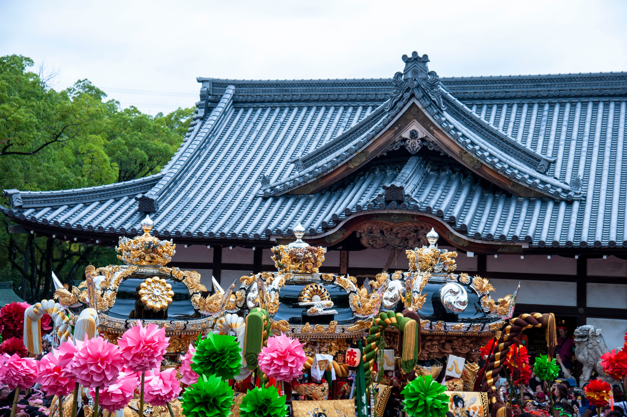 Traditional temple roof with ornate carvings and gold decorations, during a festival with colorful paper flowers in the foreground.