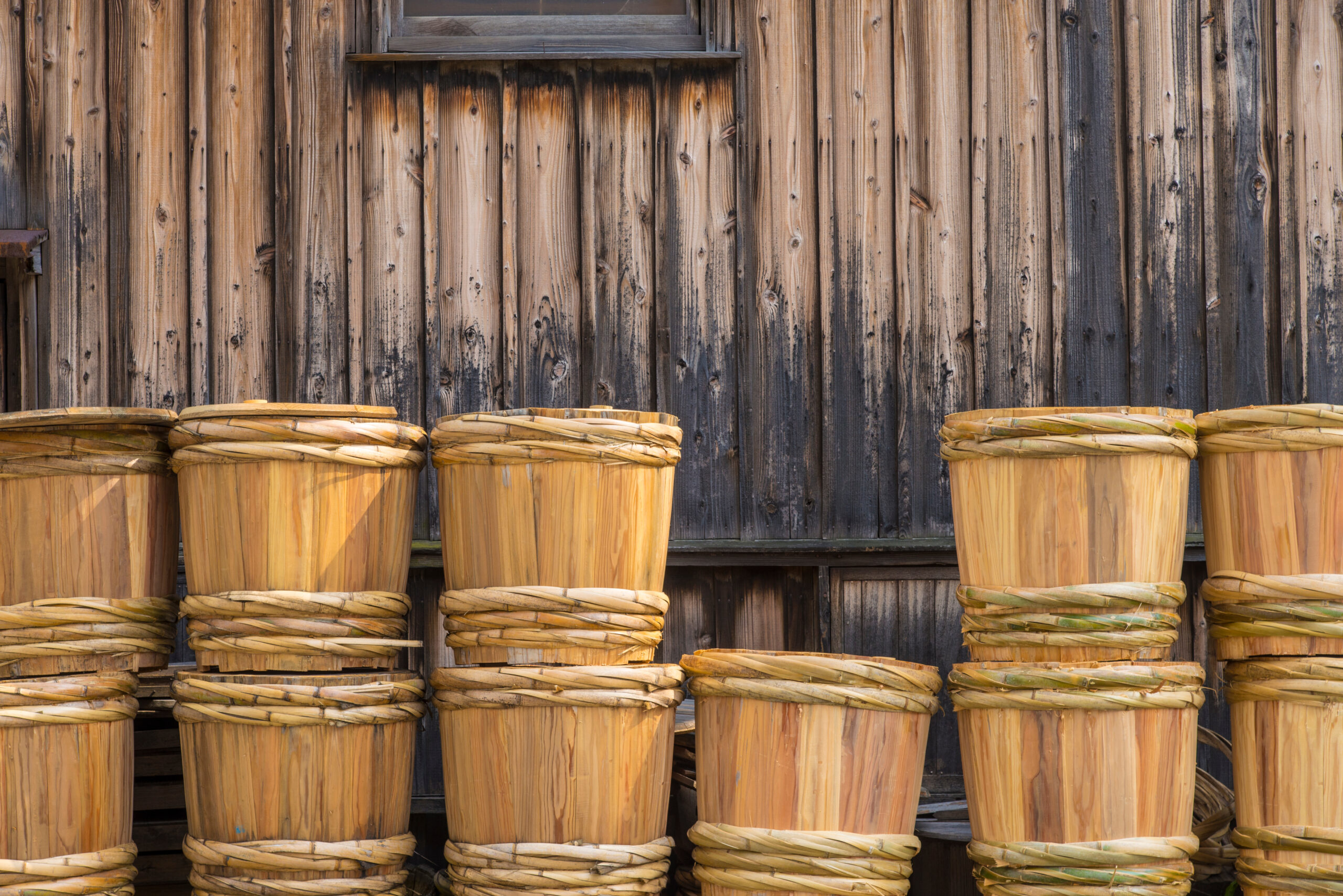 Stacks of woven wooden baskets lined up against a weathered wooden wall.