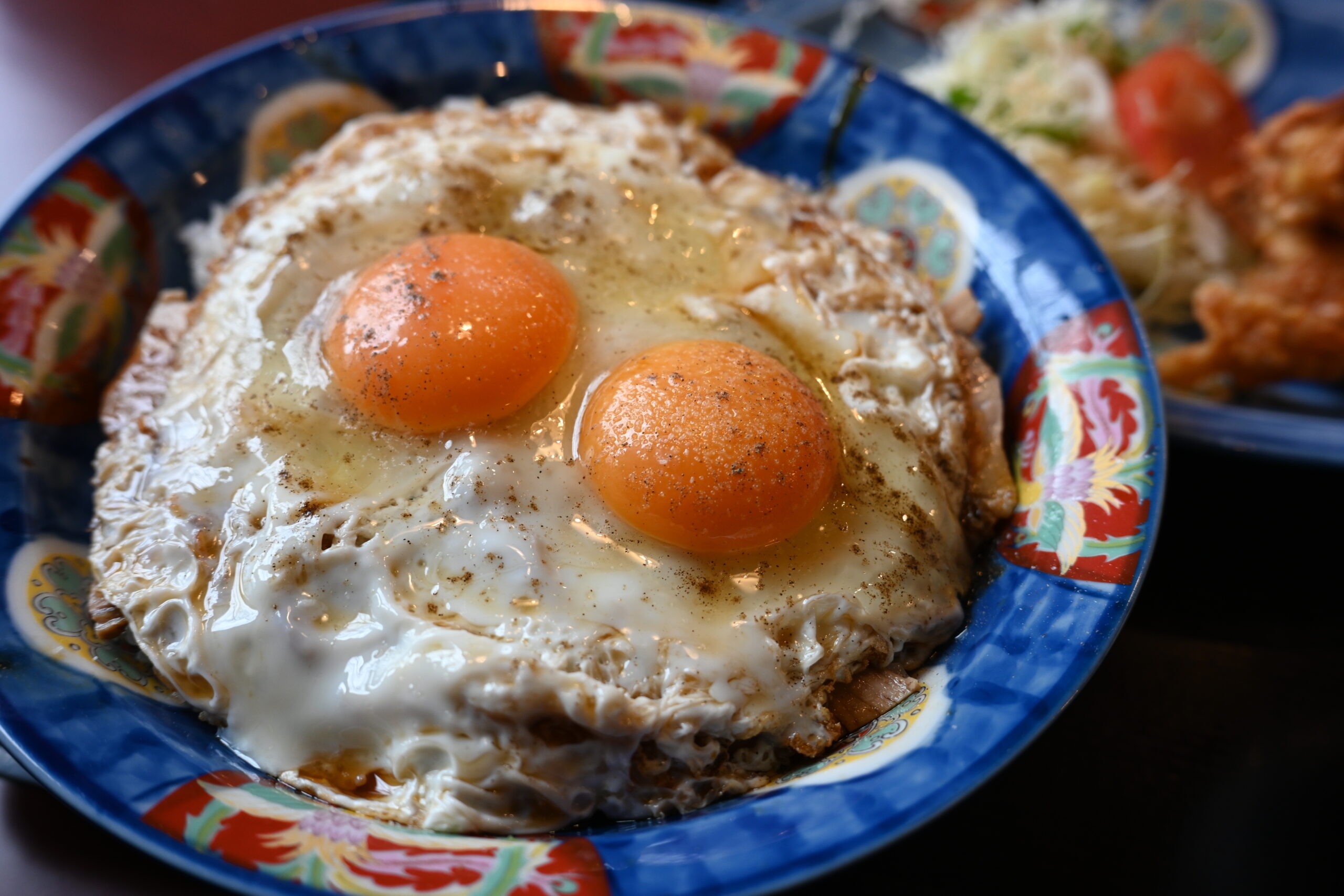 Two sunny-side-up eggs with bright orange yolks on a colorful ceramic plate.