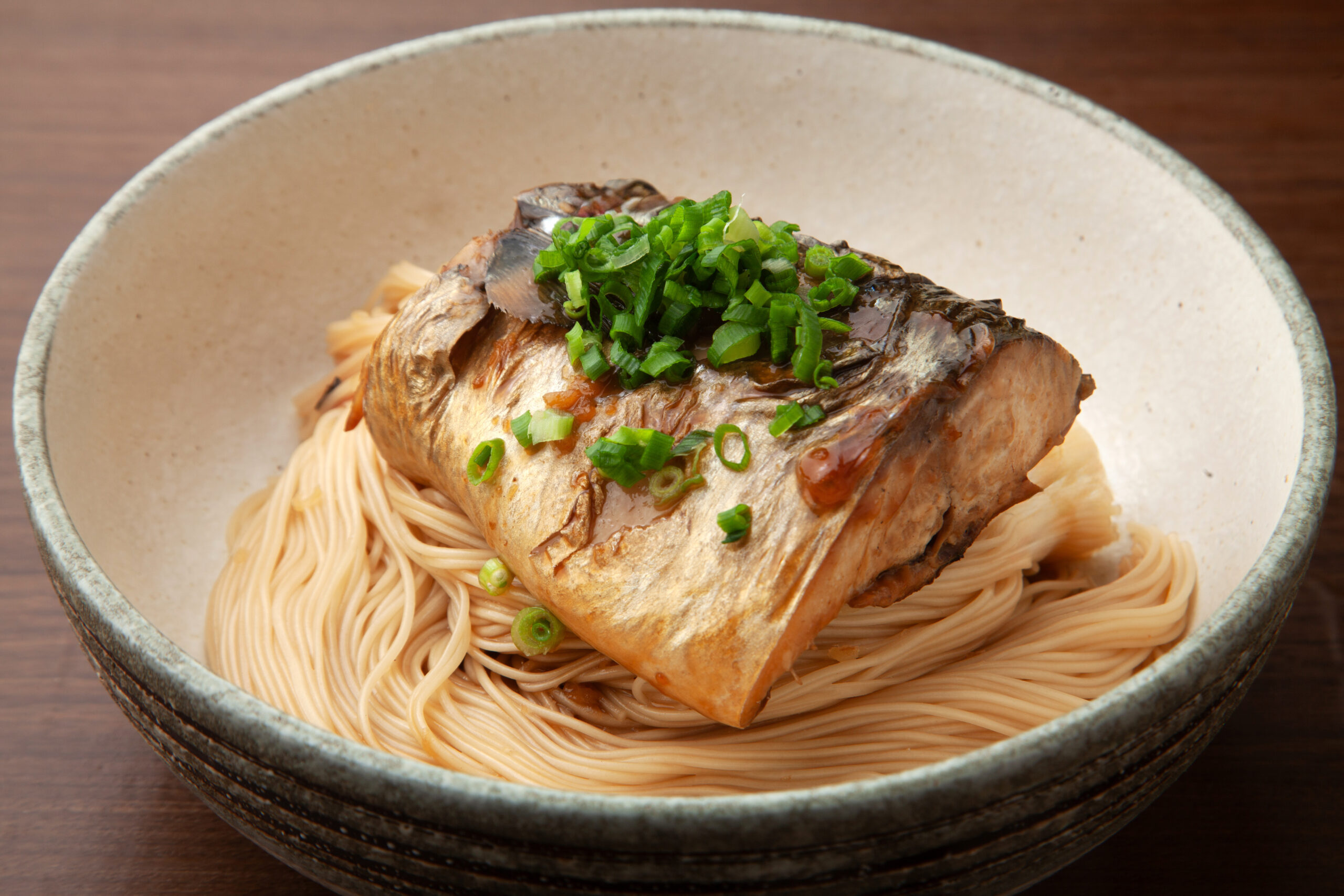 Bowl of ramen with thin noodles topped by a braised fish fillet and chopped green onions