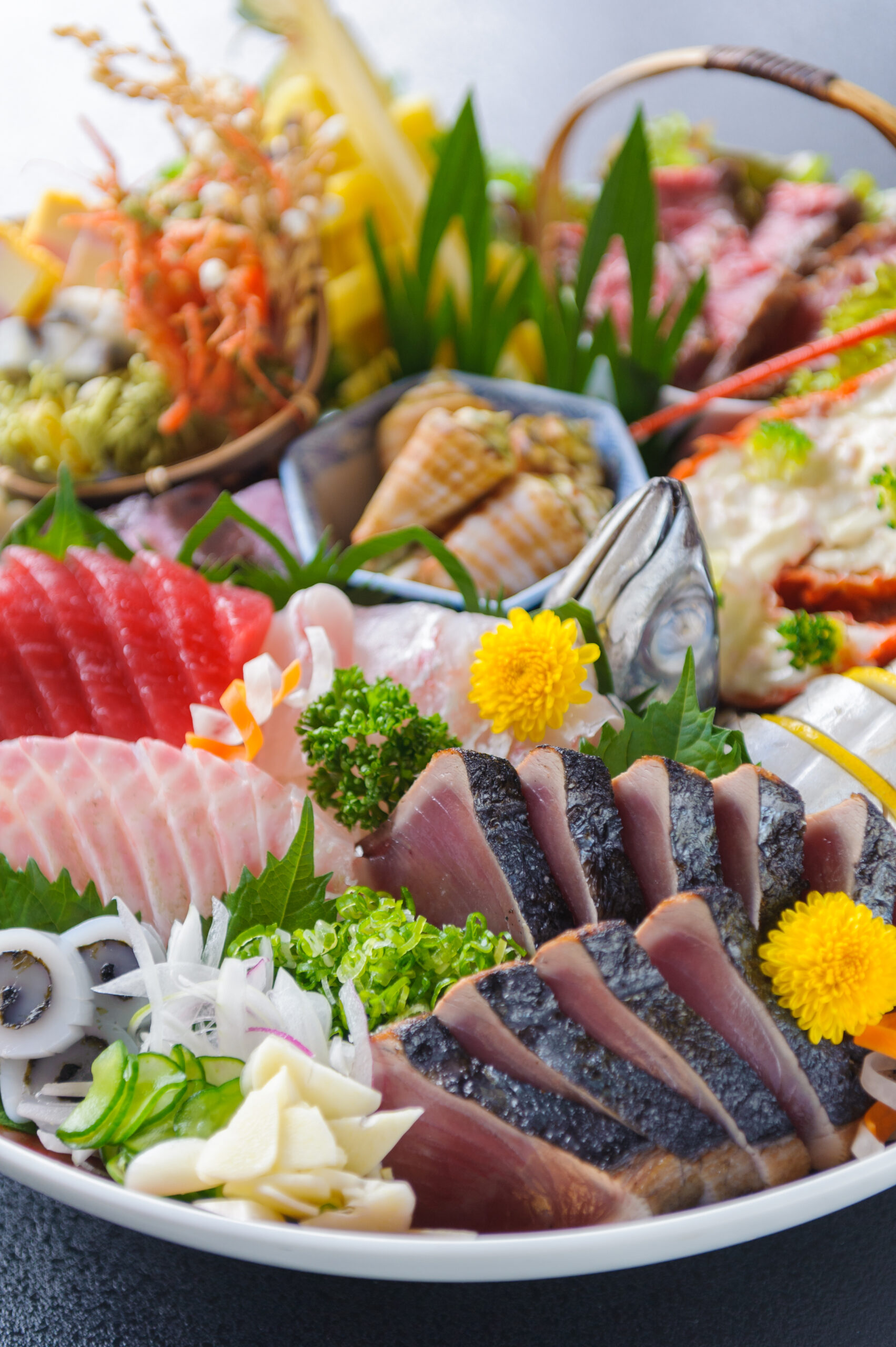 Plate of assorted sashimi with slices of tuna and other fish, arranged with greens, shredded radish, and yellow chrysanthemum blossoms as garnish.