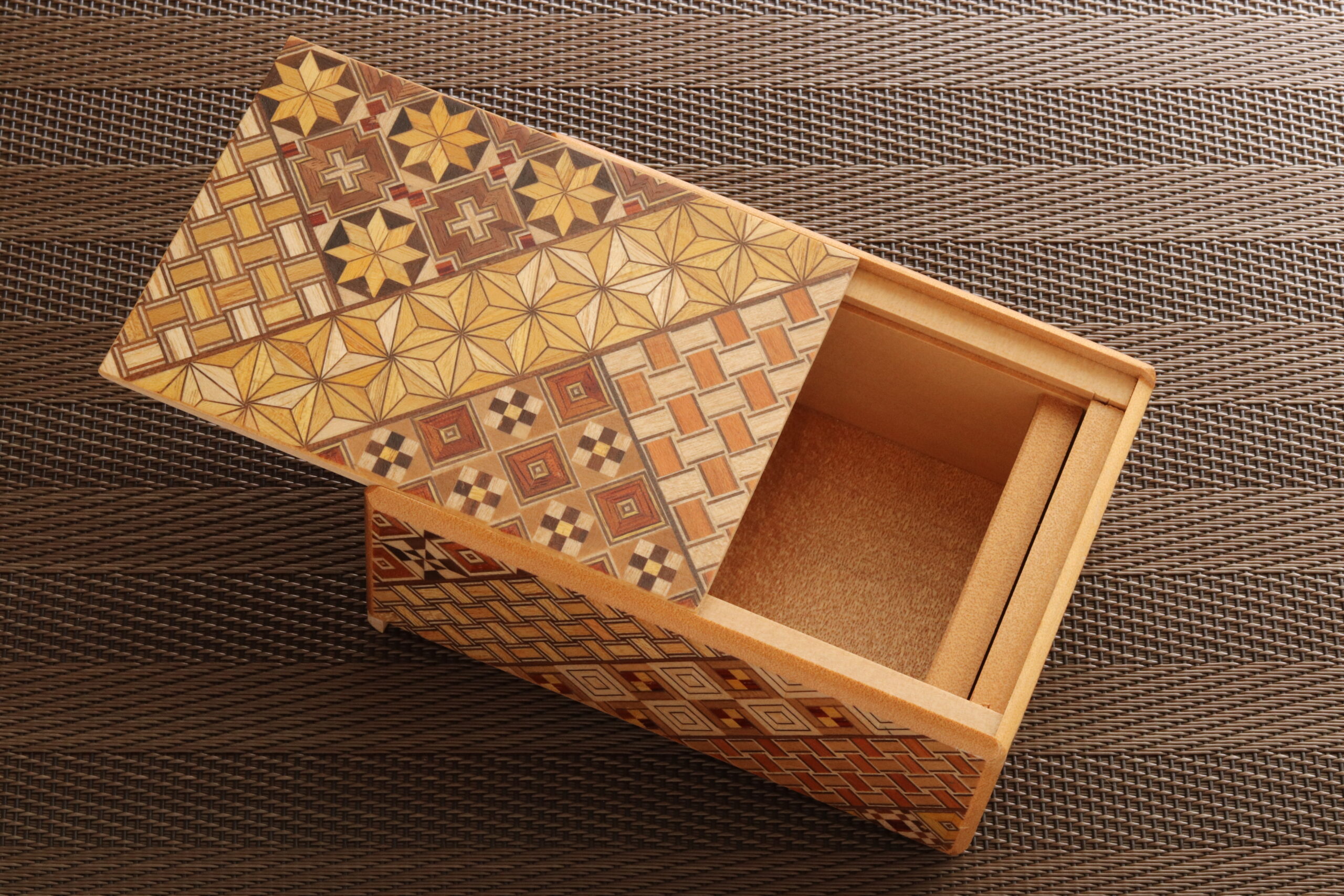 Decorative wooden box with a geometric patterned lid on a woven brown mat.