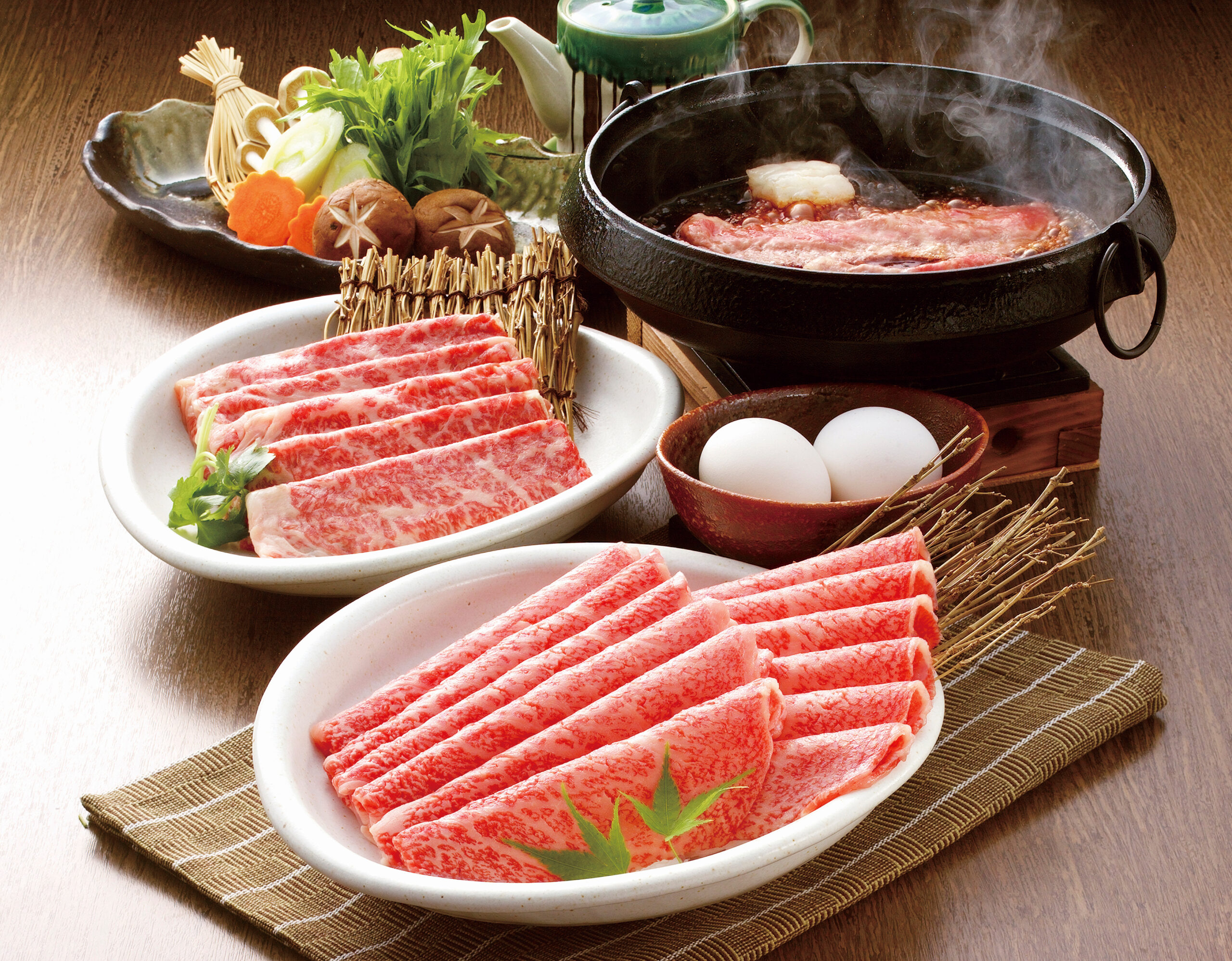 Plate of thinly sliced marbled beef ready for hot pot, with greens for garnish on a wooden table.