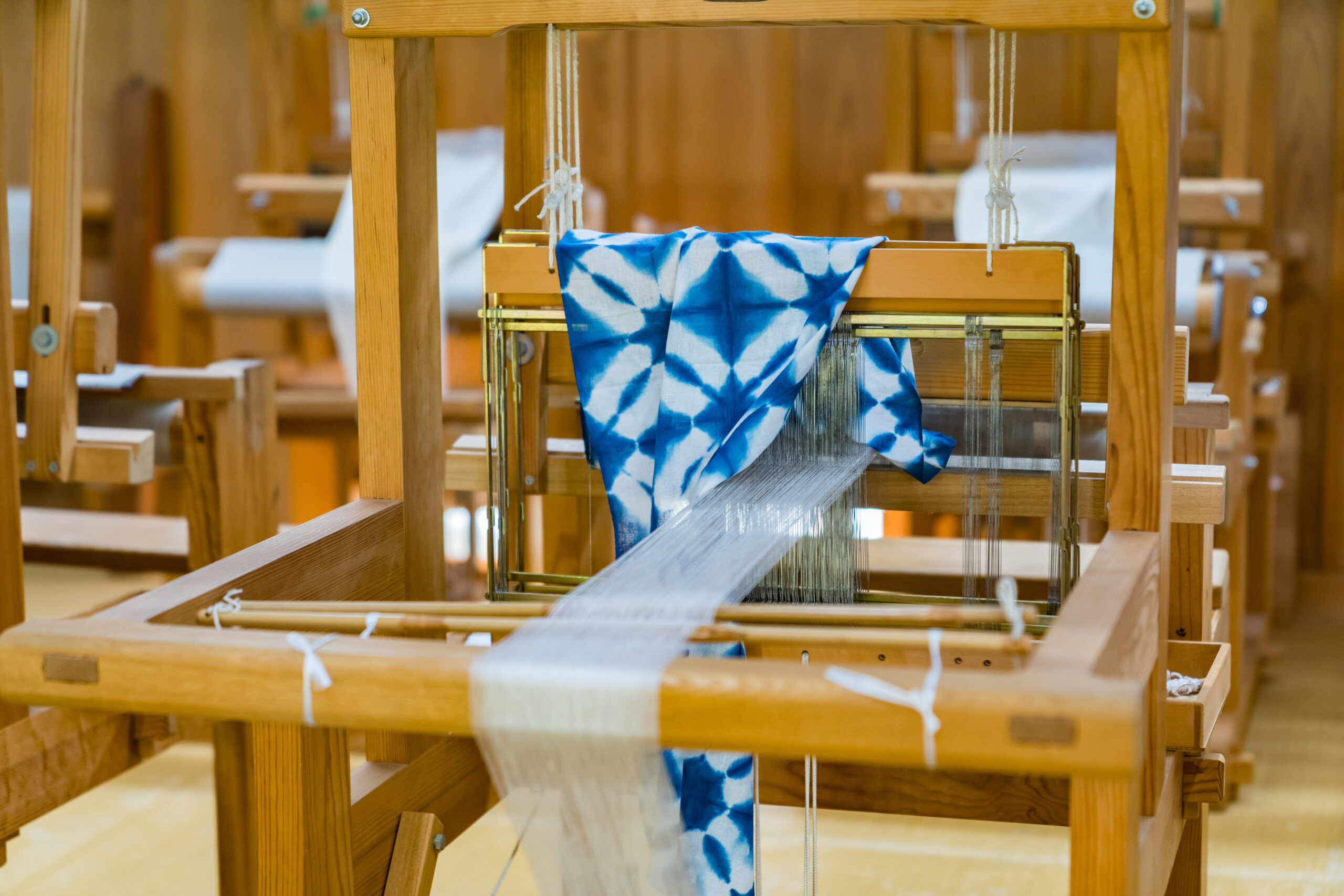 Wooden loom with a blue and white tie-dye fabric being woven in progress