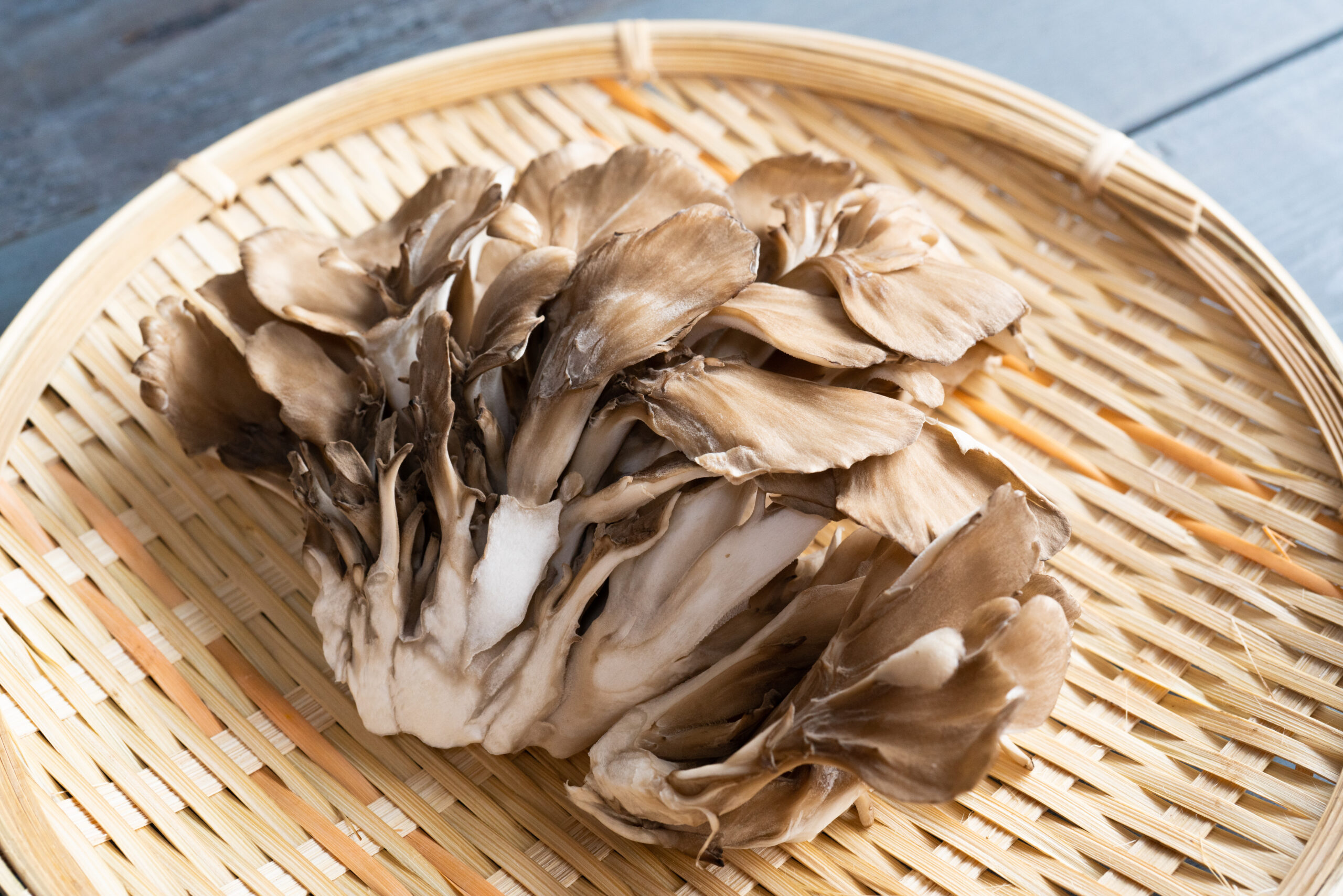 Brown oyster mushrooms piled in a round wicker basket on a wooden surface.