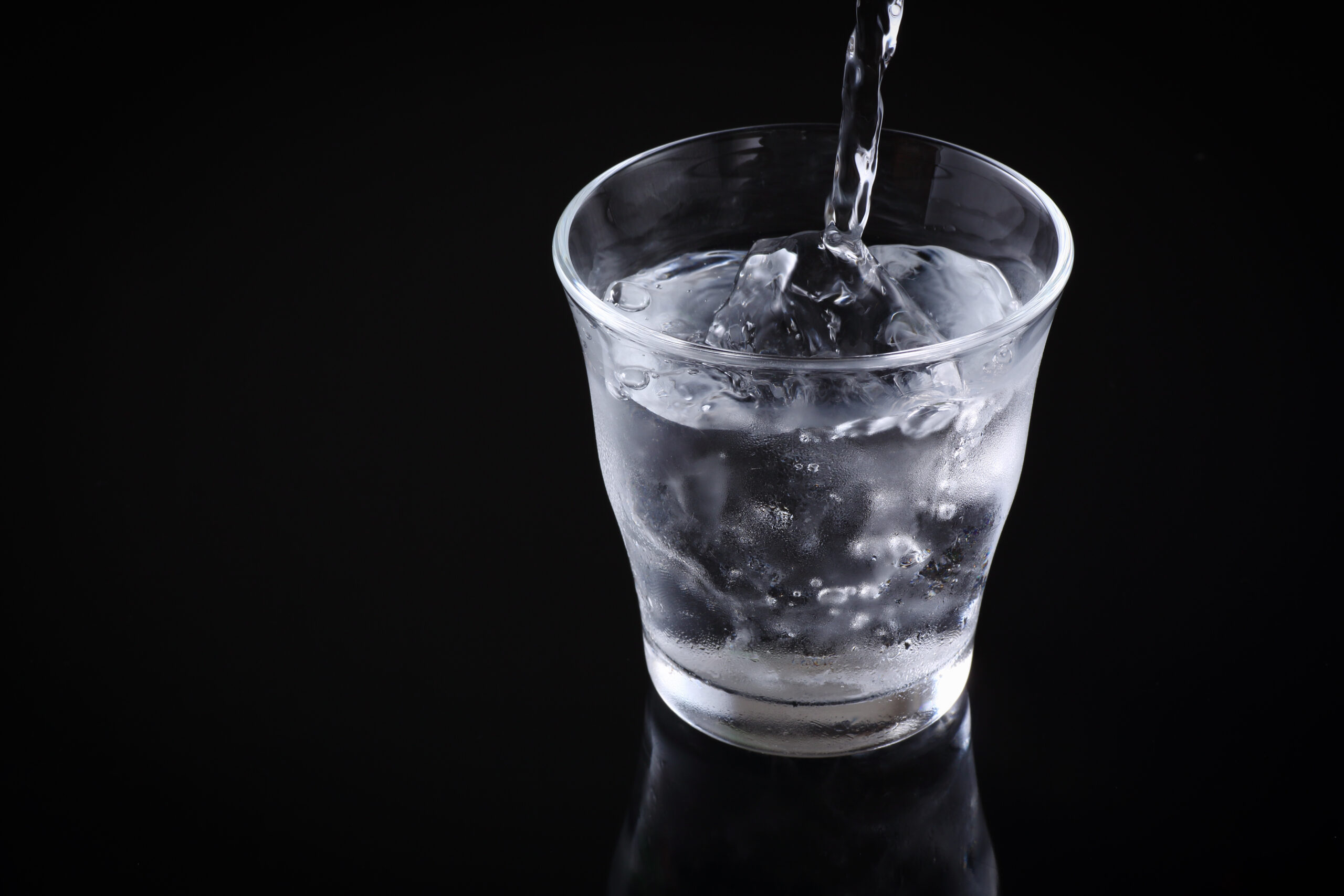 Close-up of a glass filled with ice and water as water is poured in, against a black background.