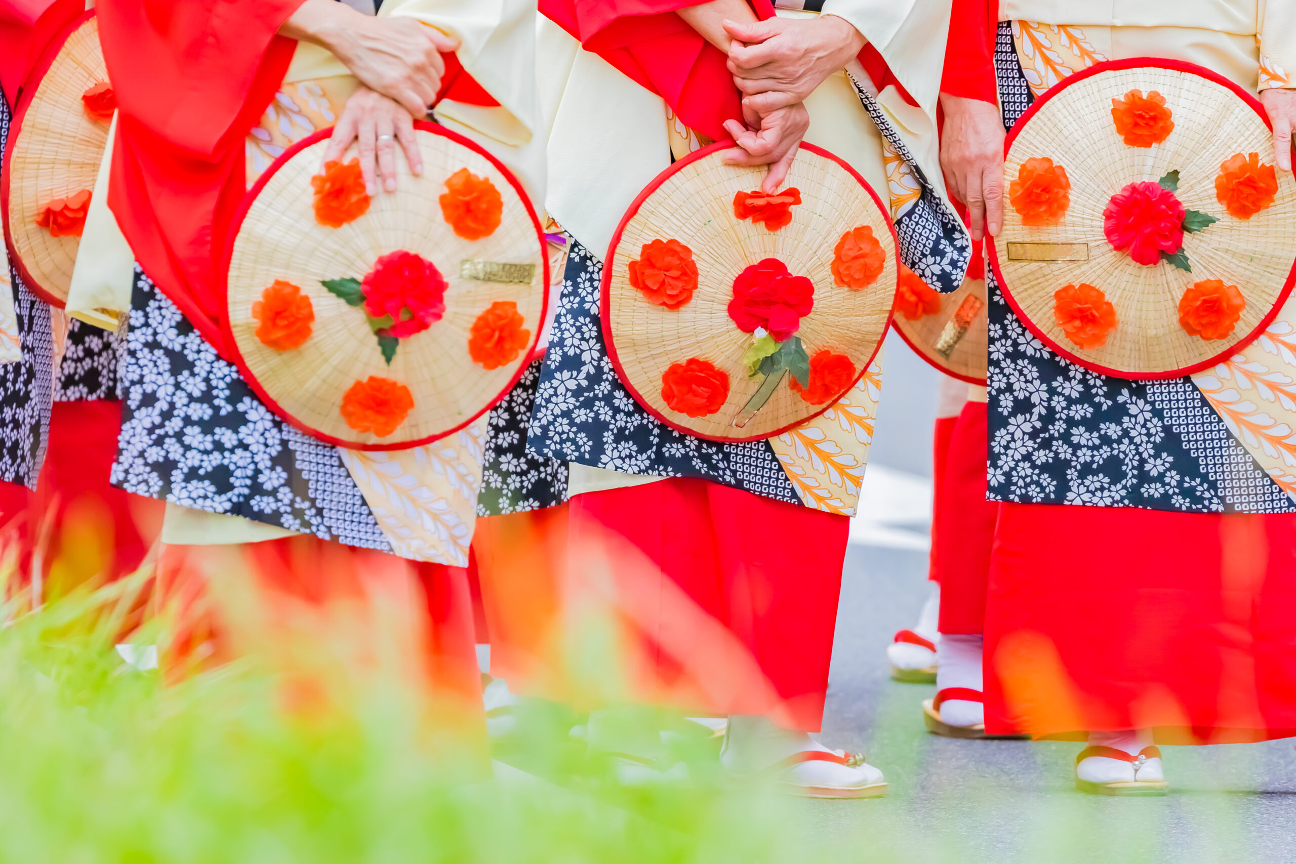 Group of dancers in bright red outfits holding decorative round straw hats with orange flowers during a festival.