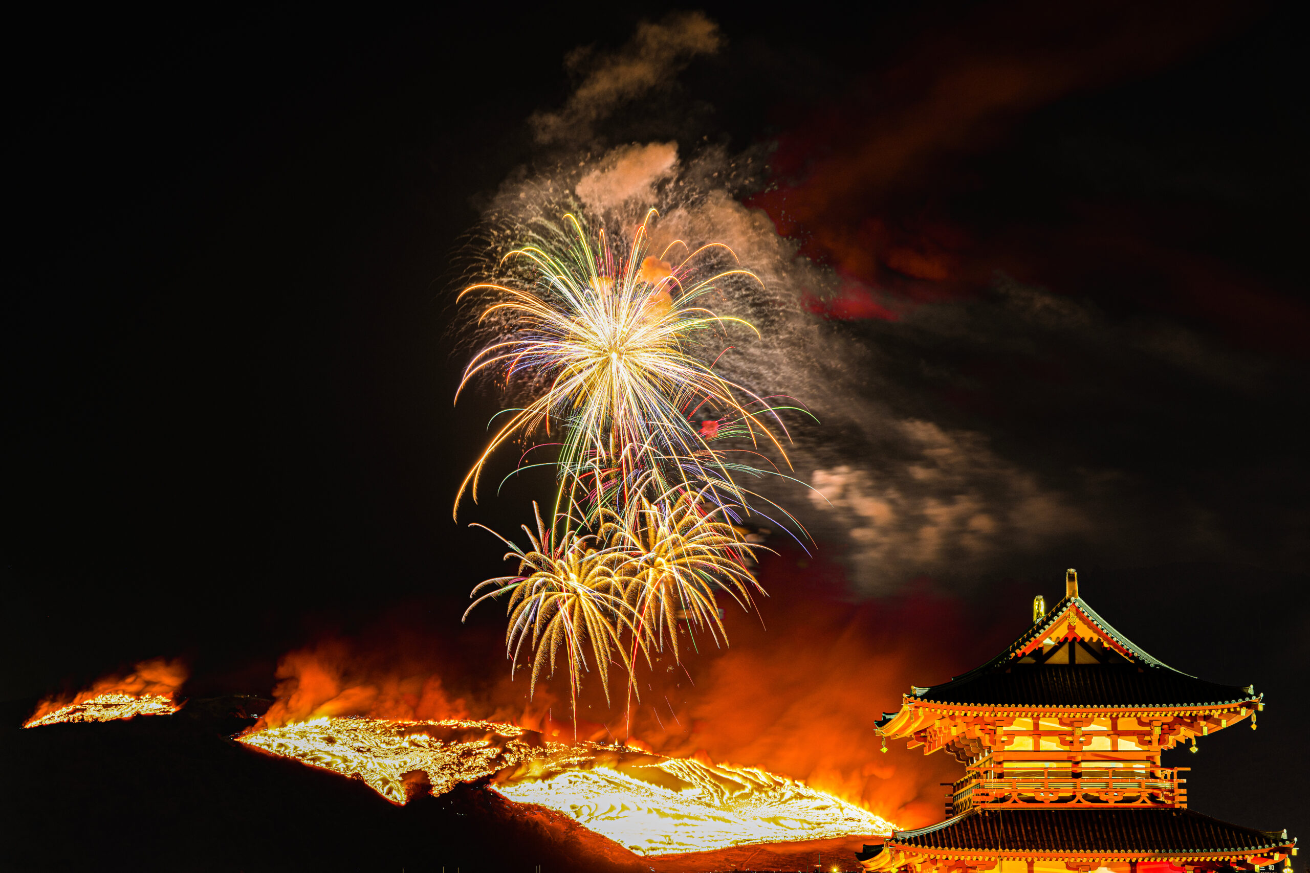 Night scene with colorful fireworks above a traditional pagoda-style temple roof against a dark sky, celebrating a festival.