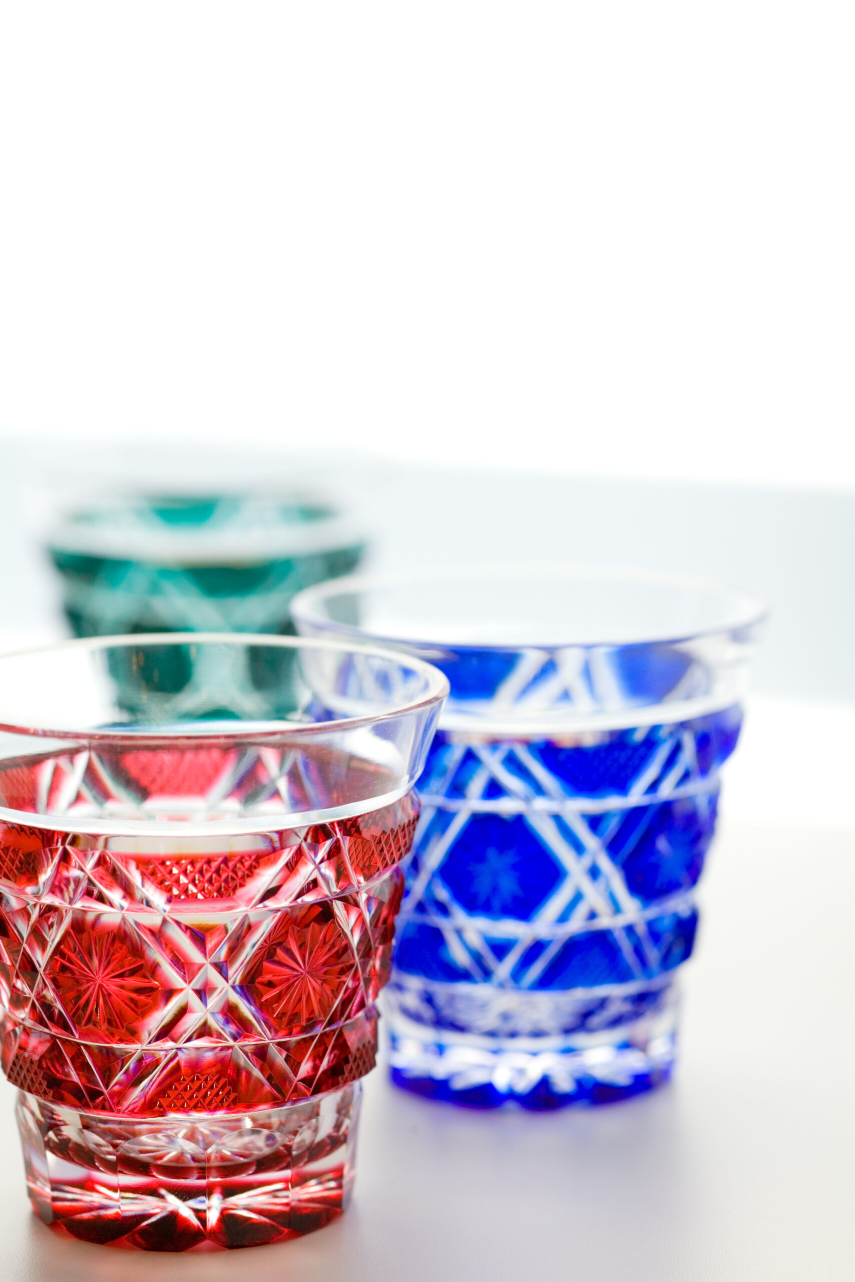 Close-up of red and blue cut-crystal glasses with intricate geometric patterns on a white surface.