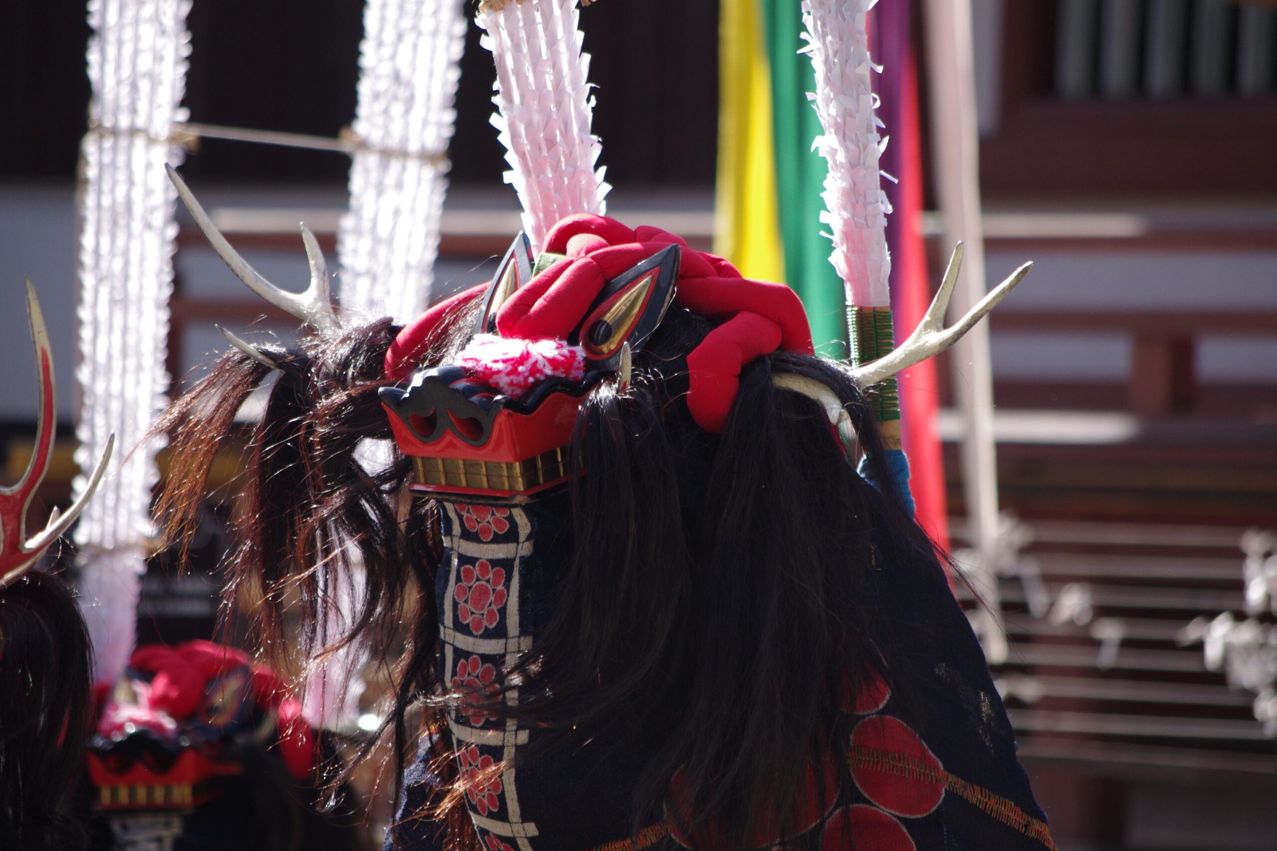 Close-up of a ceremonial headpiece with red fabric, faux antlers, and white tassels worn in a festival parade