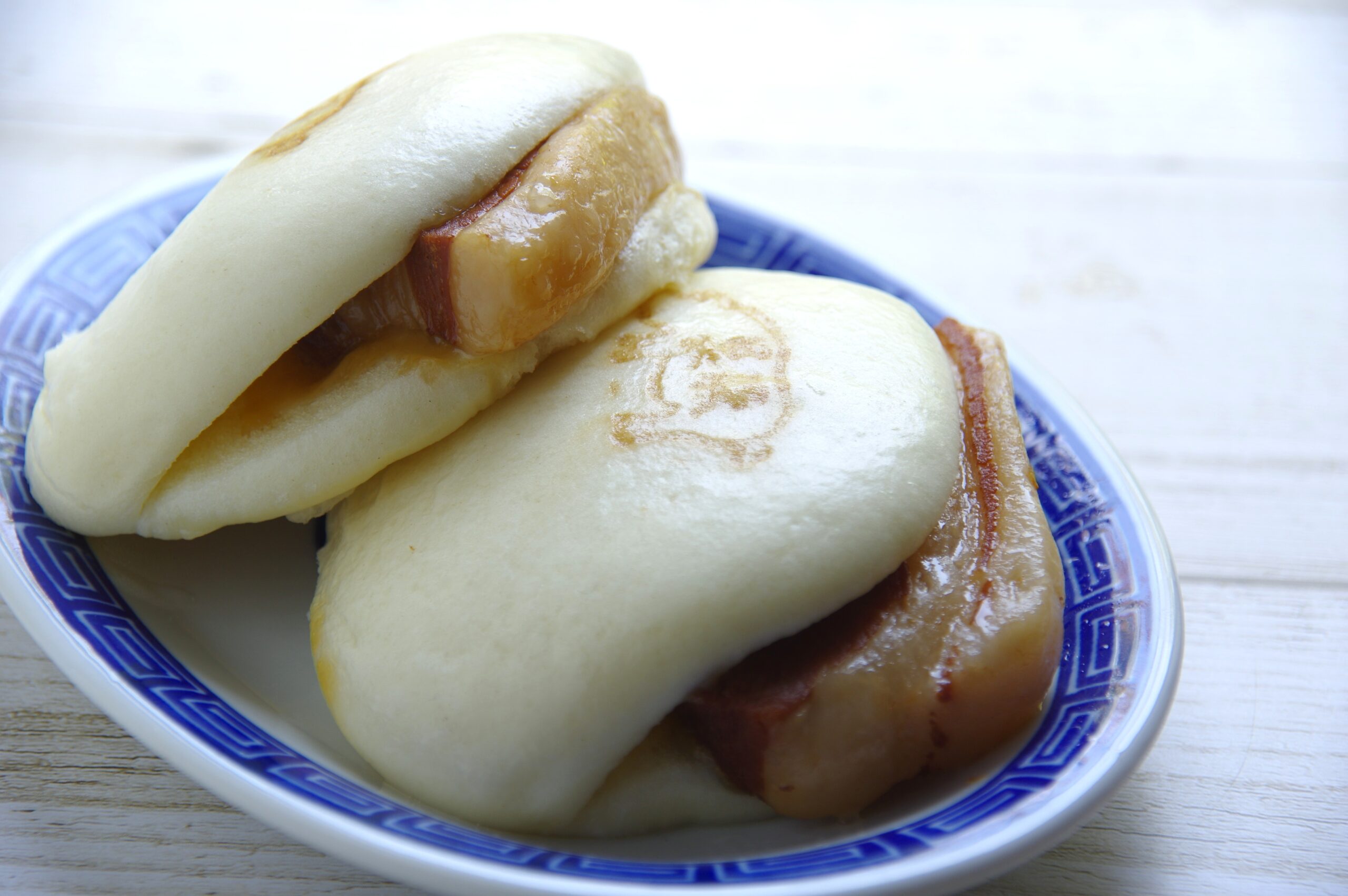 Soft steamed buns with hot dogs peeking out, served on a blue patterned plate.