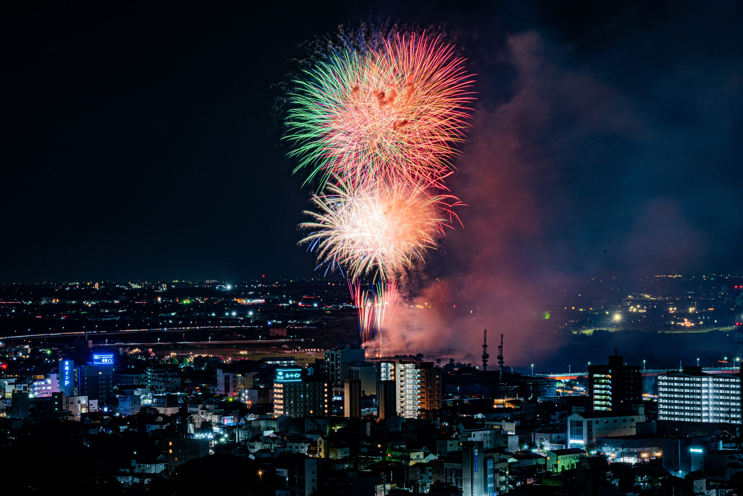 Night city skyline beneath colorful fireworks bursting in the night sky over a cityscape.