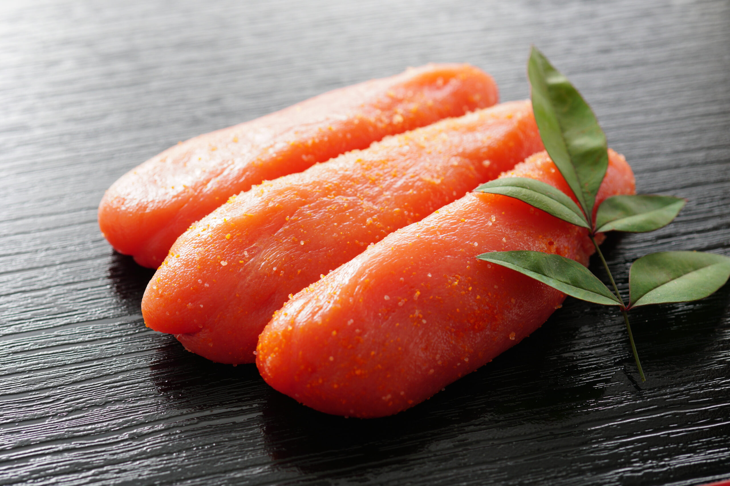 Raw salmon fillets sprinkled with salt on a dark wooden board, with green leaves garnish.