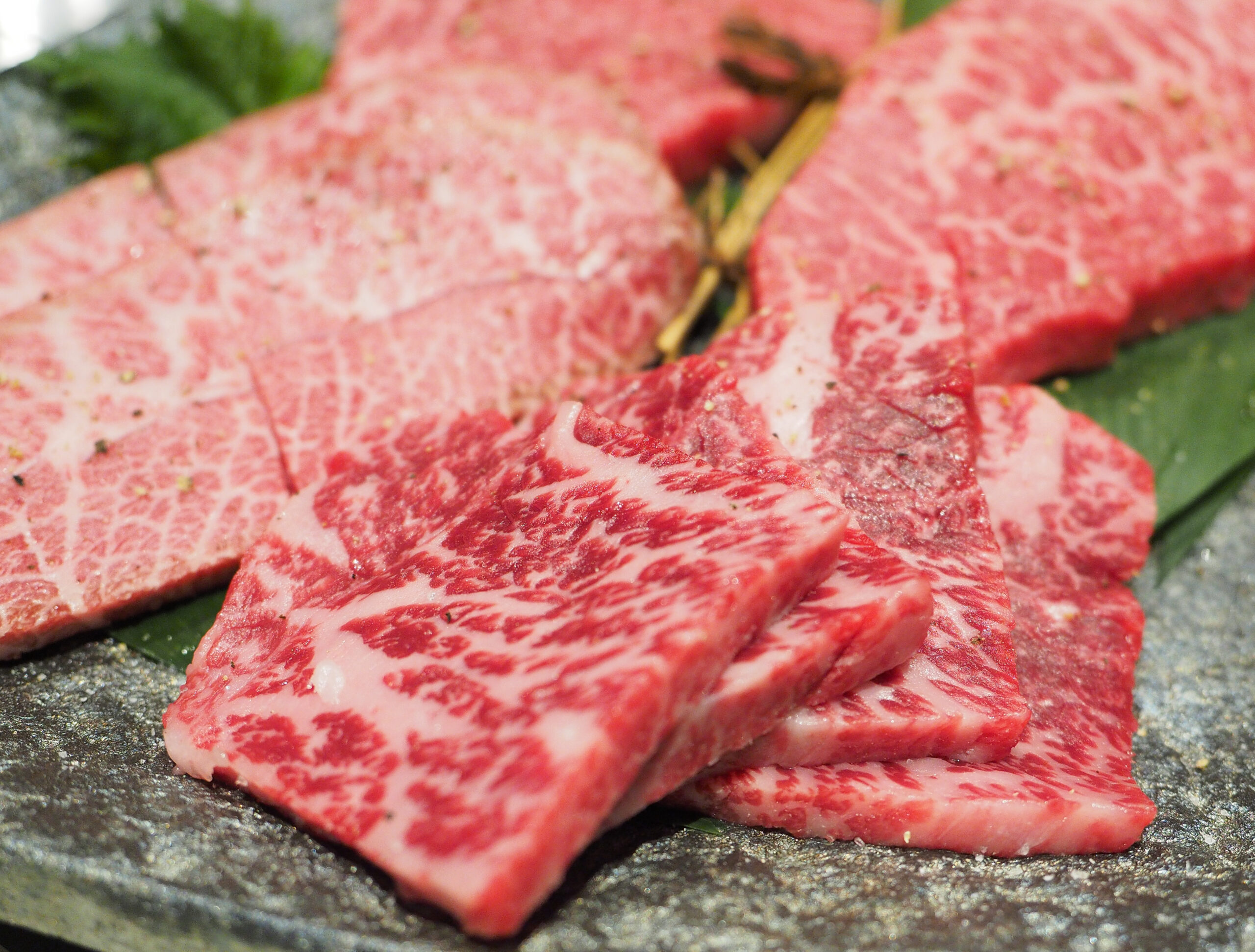 Thinly sliced, heavily marbled raw beef on a dark stone surface, ready to cook.