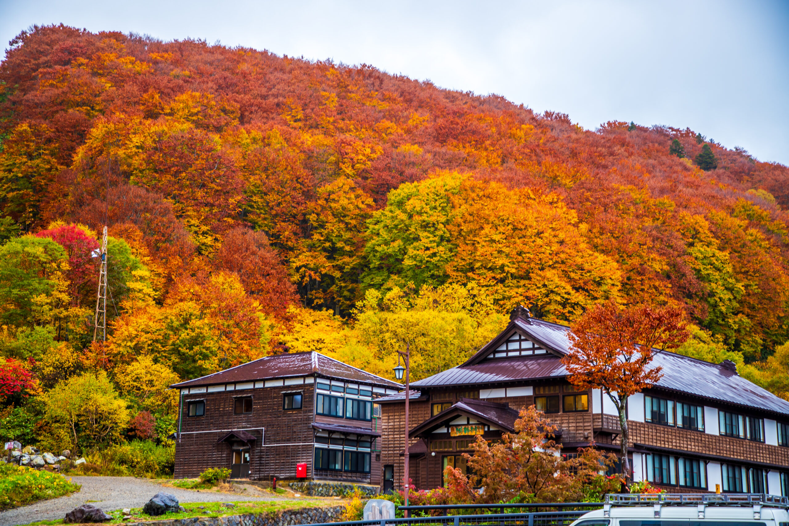 Two-story wooden lodge with brown roof at the base of a forested hill in vivid fall colors,