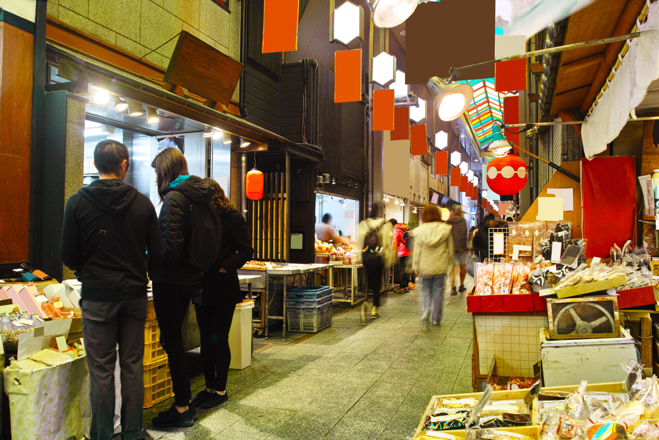 Busy indoor market alley with stalls selling goods, shoppers walking and browsing under colorful lanterns and signs