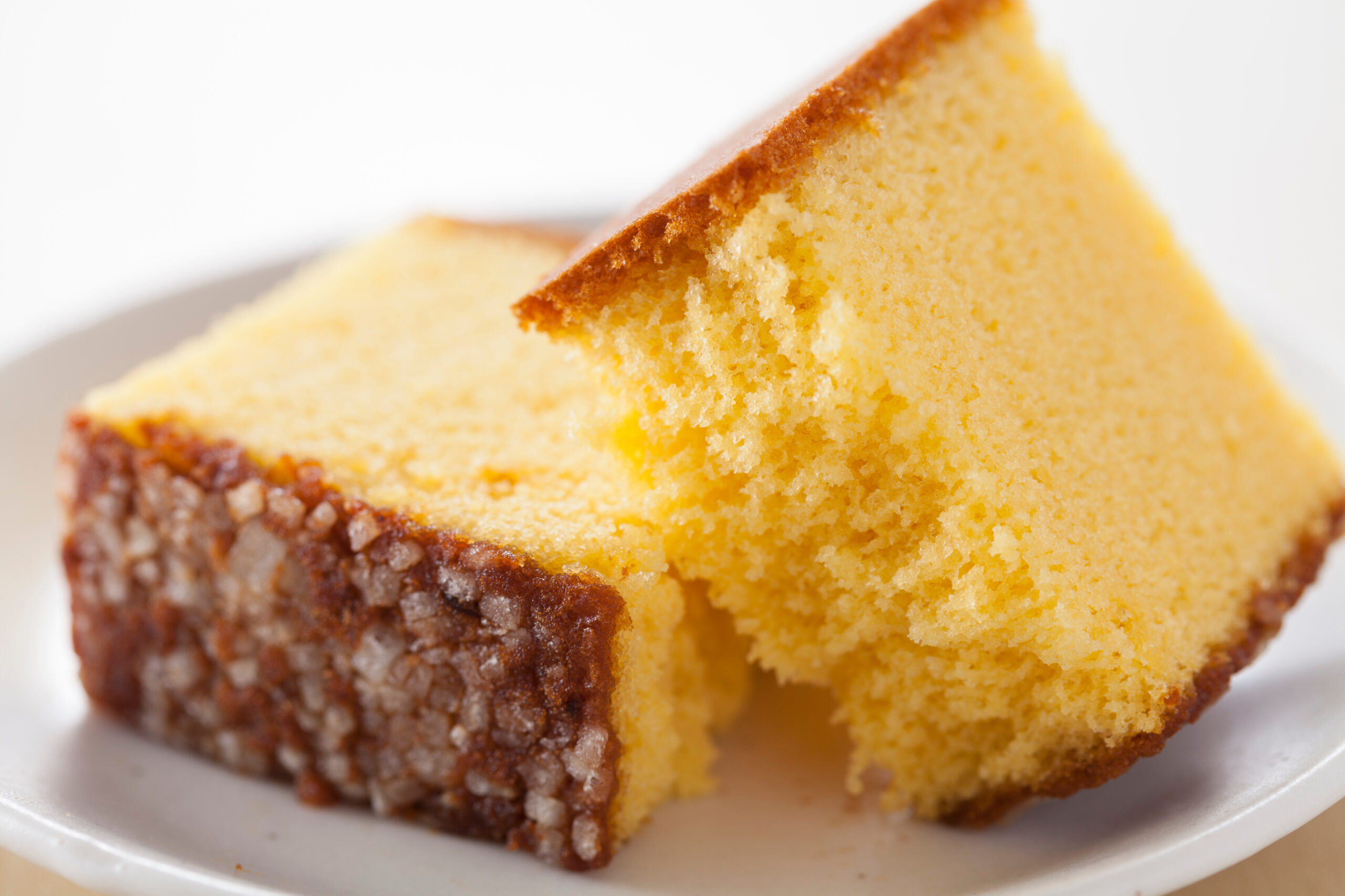 Close-up of a slice of yellow pound cake with a sugary crust on a white plate.