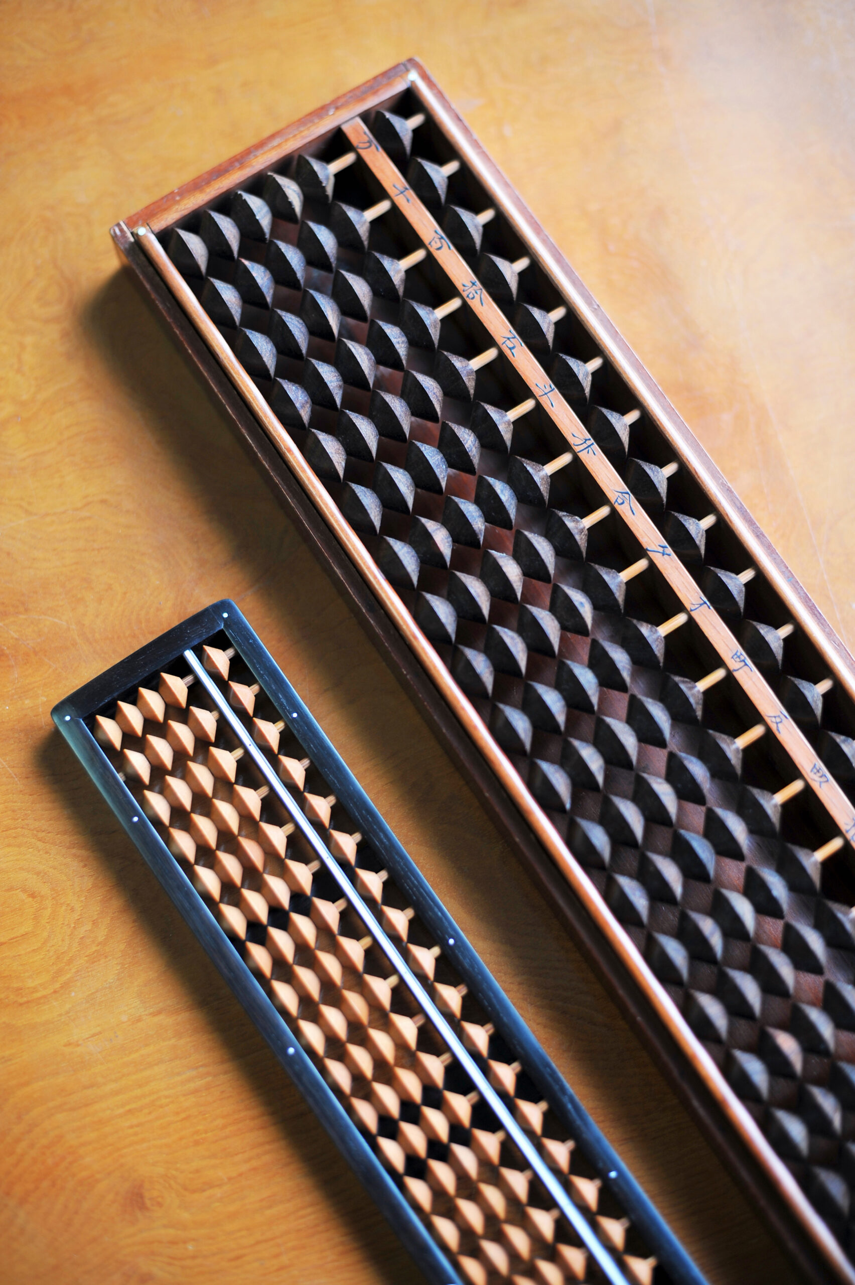 Tilted view of two wooden abacuses with rows of beads resting on a wooden table, one blue-framed and one brown-framed.