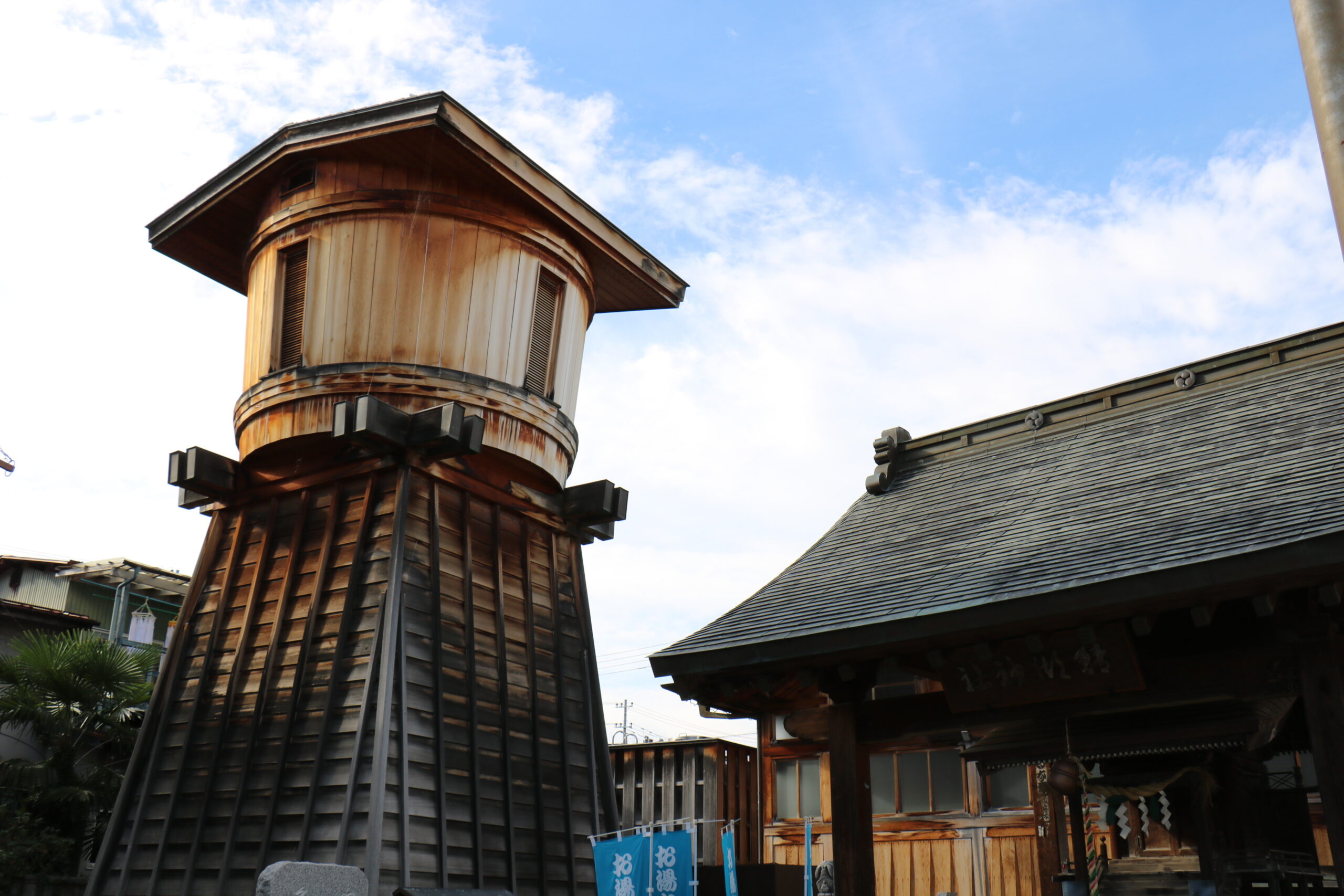 Wooden tower of a traditional Japanese building with curved eaves and vertical slats against a blue sky