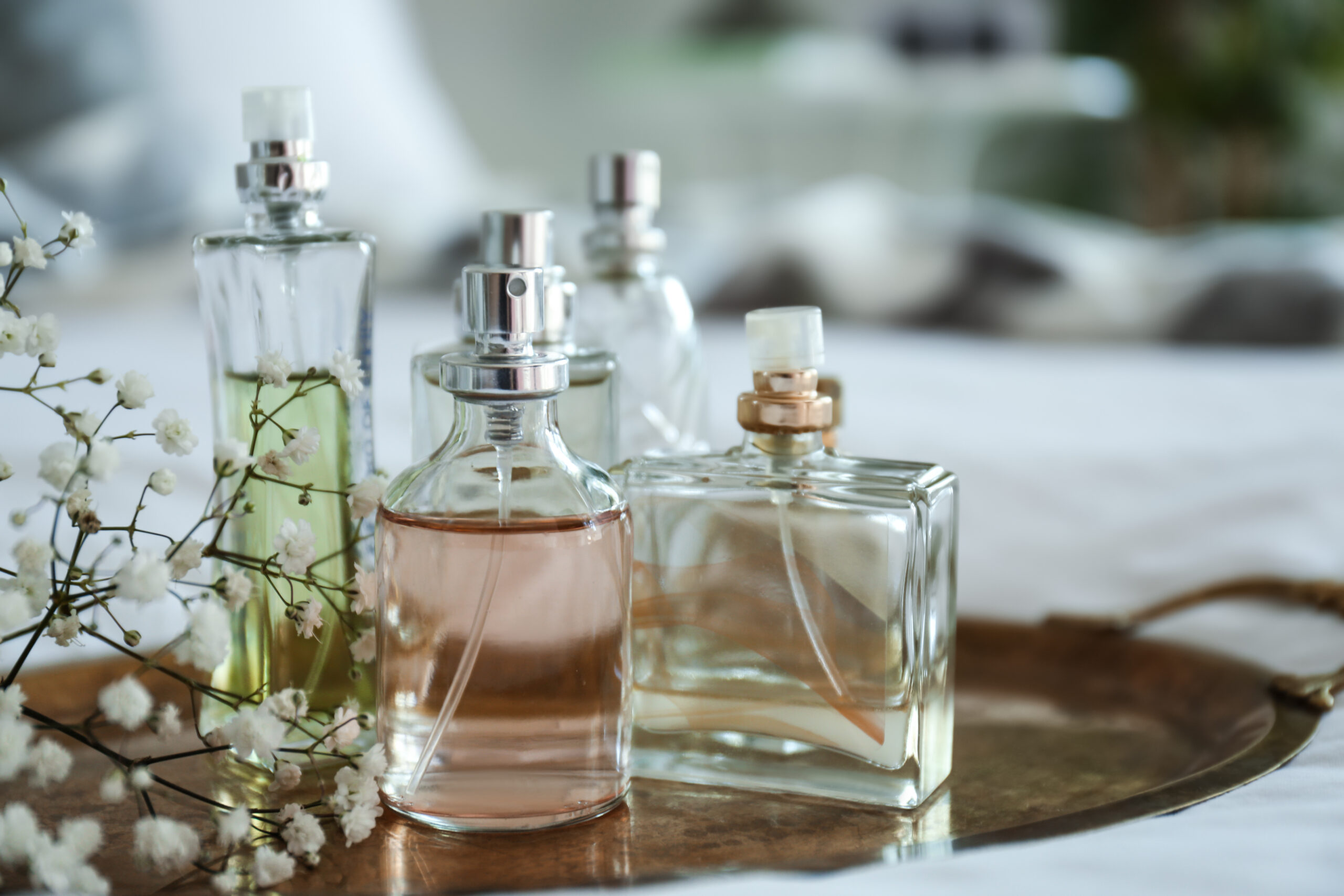 Assorted glass perfume bottles with pink and clear liquids on a wooden tray, accompanied by small white flowers (gypsophila).