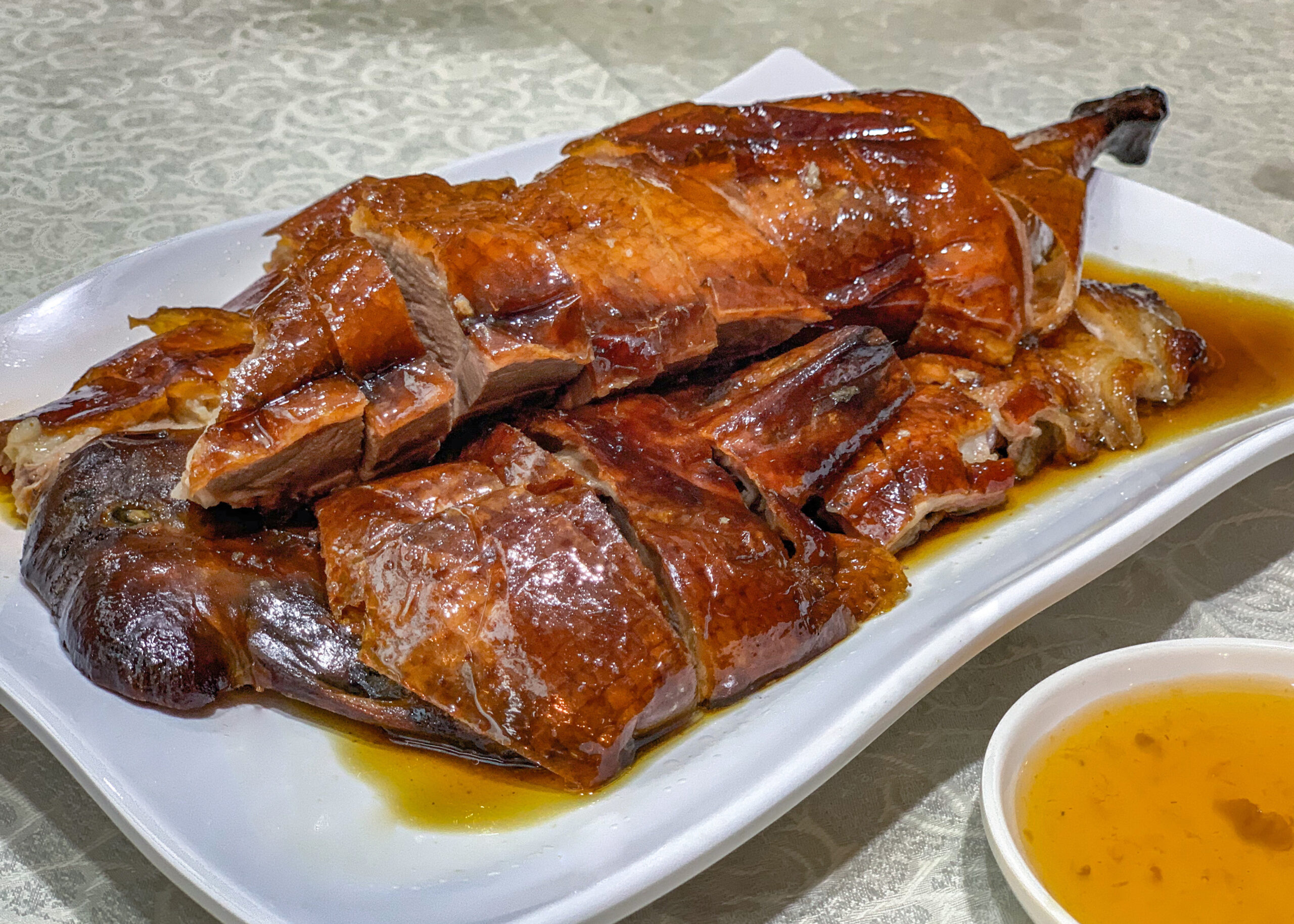 Roasted sliced duck on a white platter with orange glaze and sauce pooling around it.