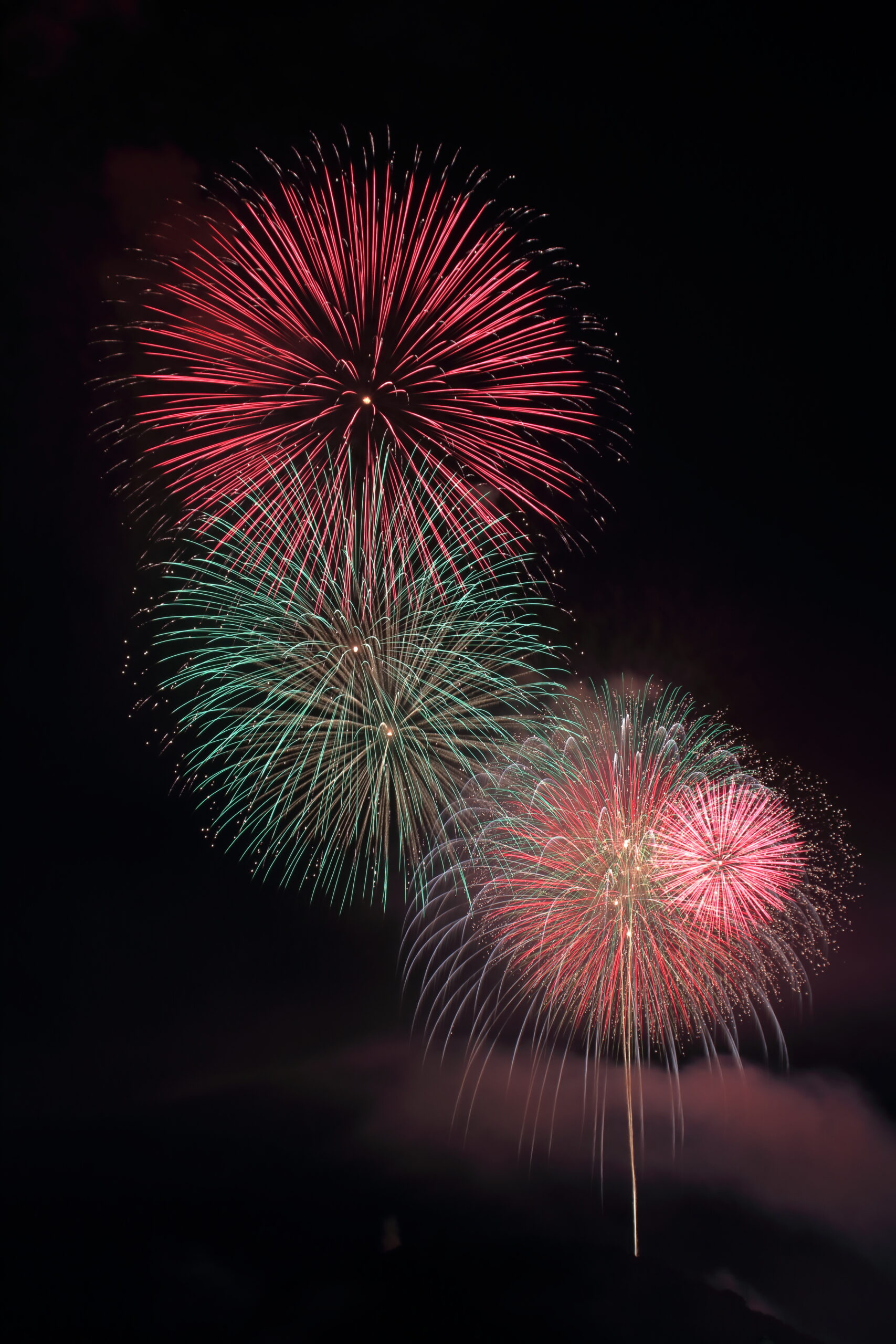 Fireworks exploding in a dark night sky with red, green, and pink bursts.