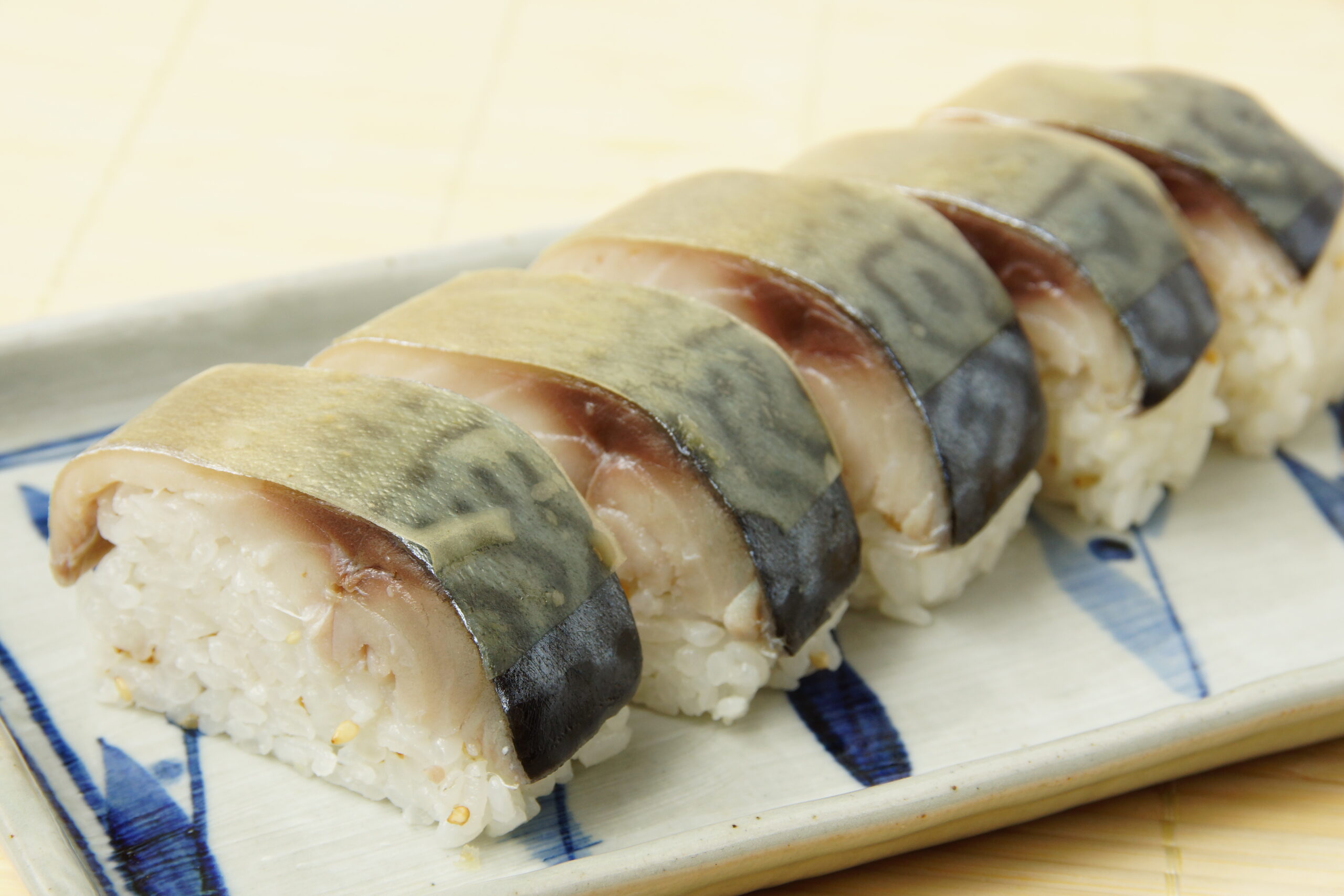 Nigiri sushi with thin fish slices draped over compact rice on a blue-patterned plate.