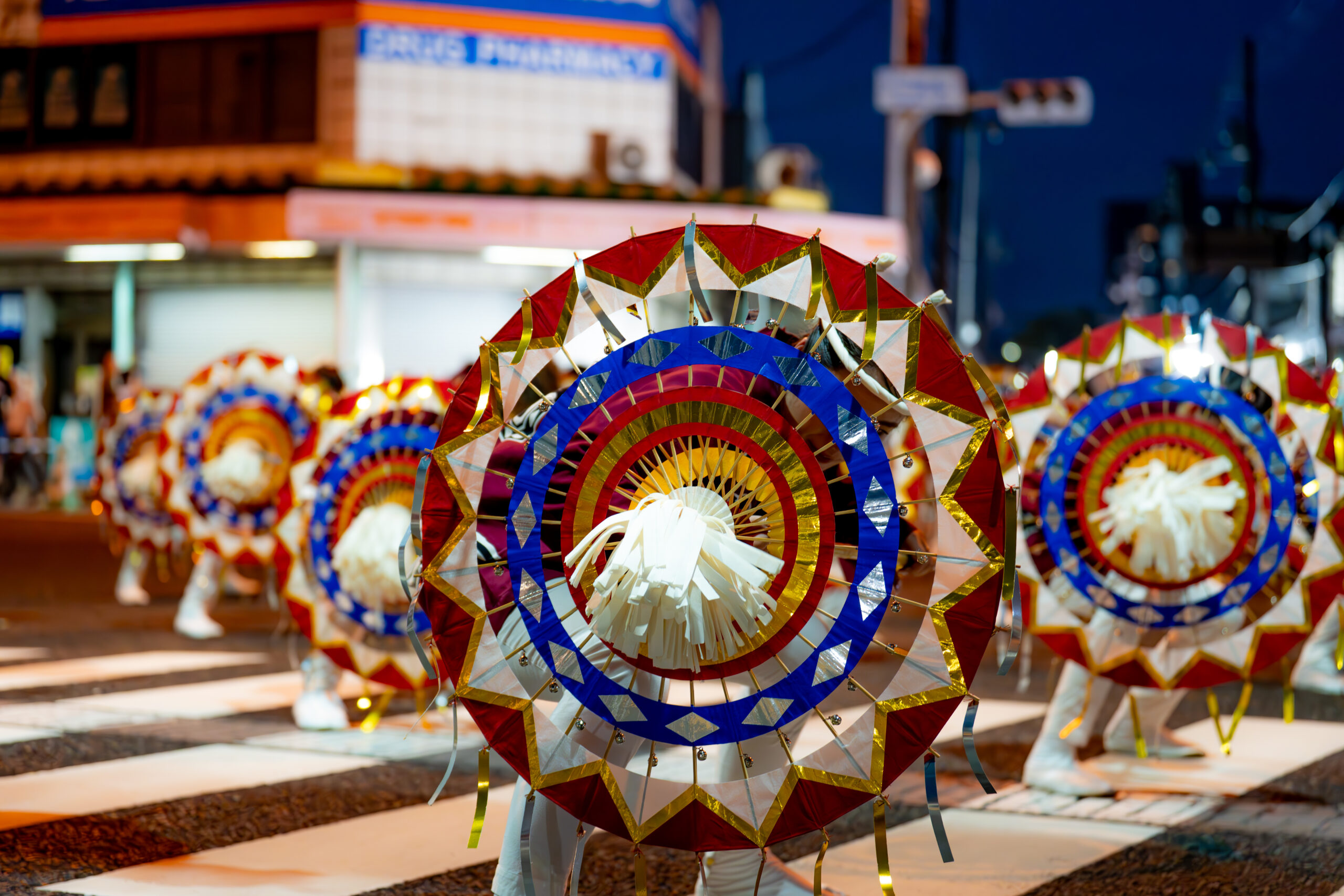 Colorful circular parade props with red, blue, and gold foil patterns during a street festival at night