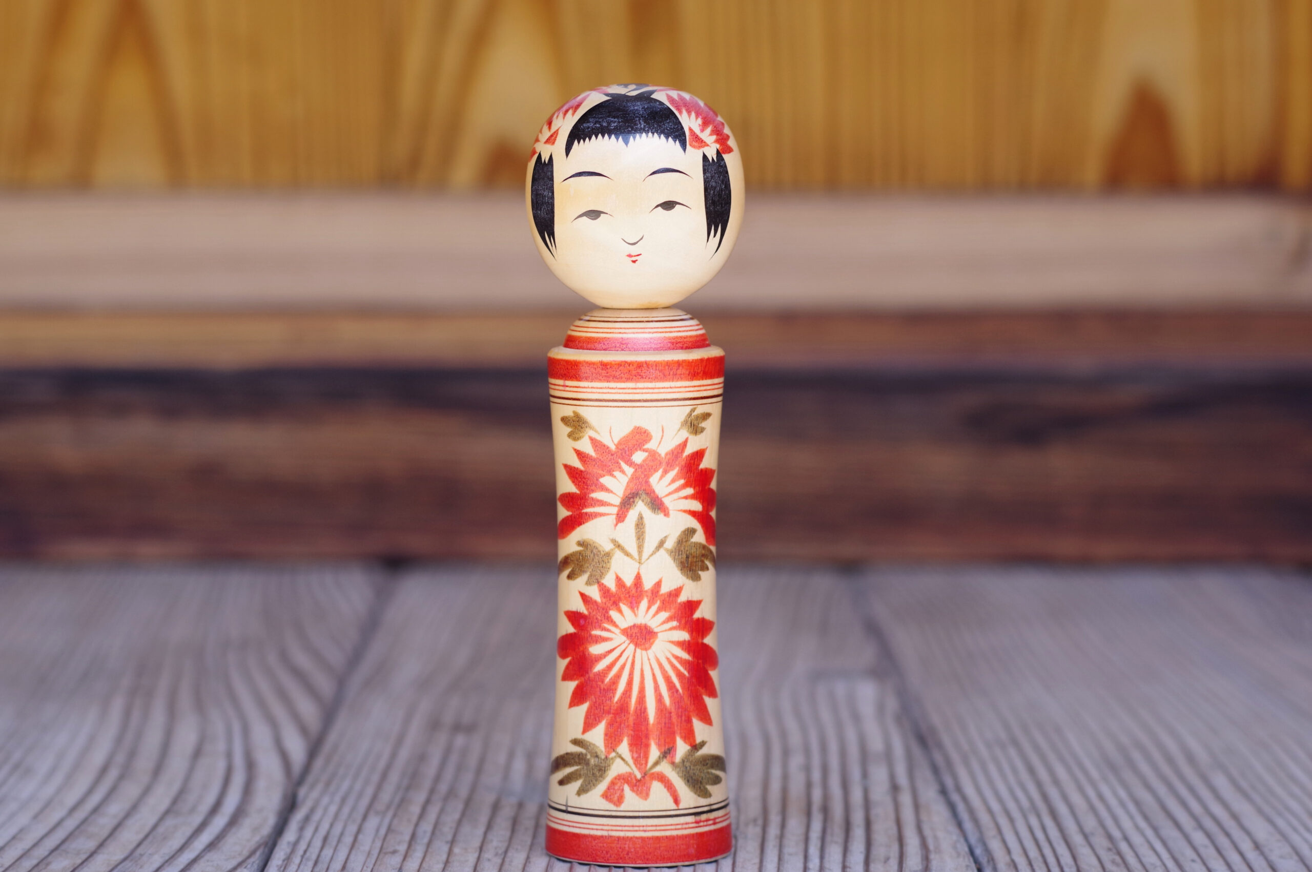Wooden kokeshi doll standing upright on a textured wooden surface with a blurred background.