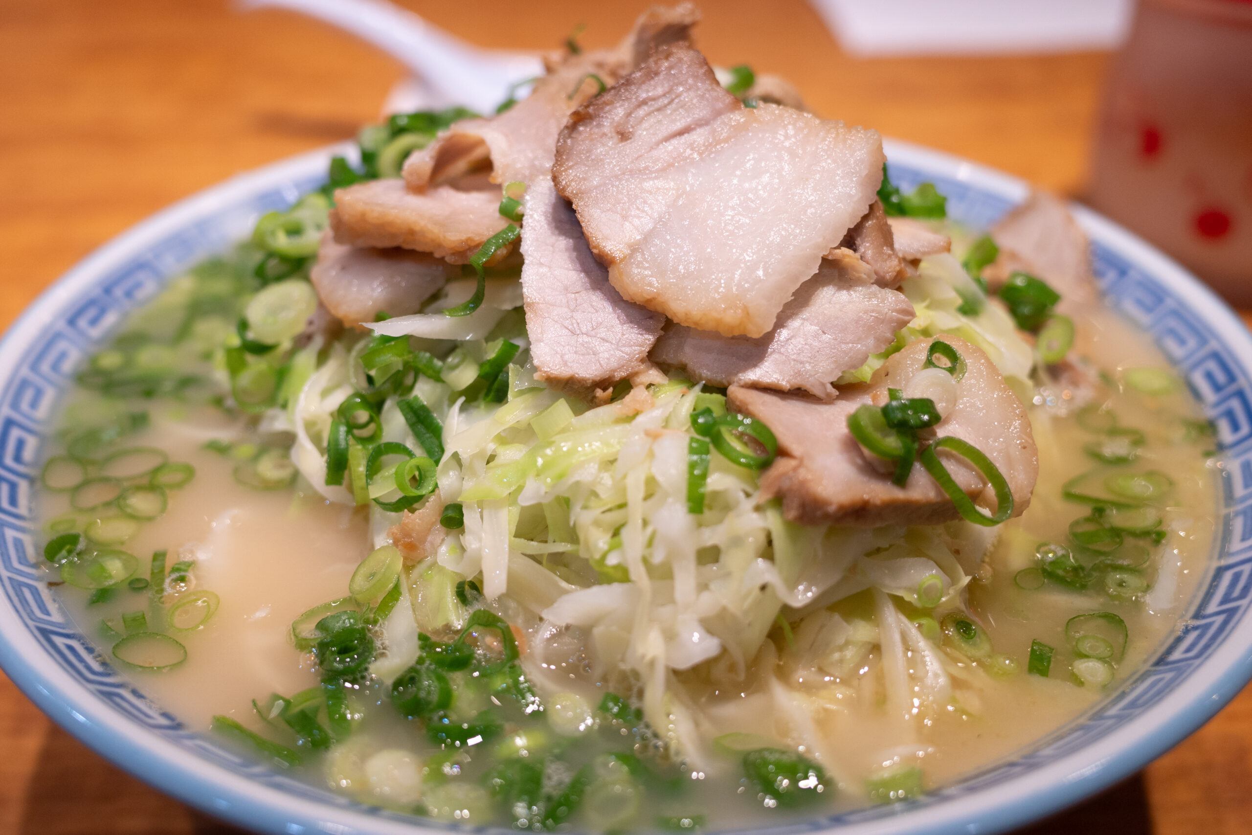 Bowl of ramen topped with sliced pork, chopped green onions, and shredded cabbage in a light broth.