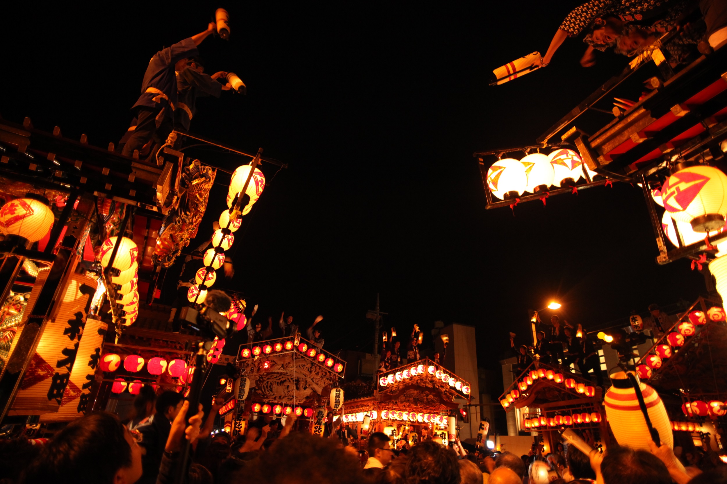 Nighttime festival scene with people on a float and glowing lanterns lining the street.