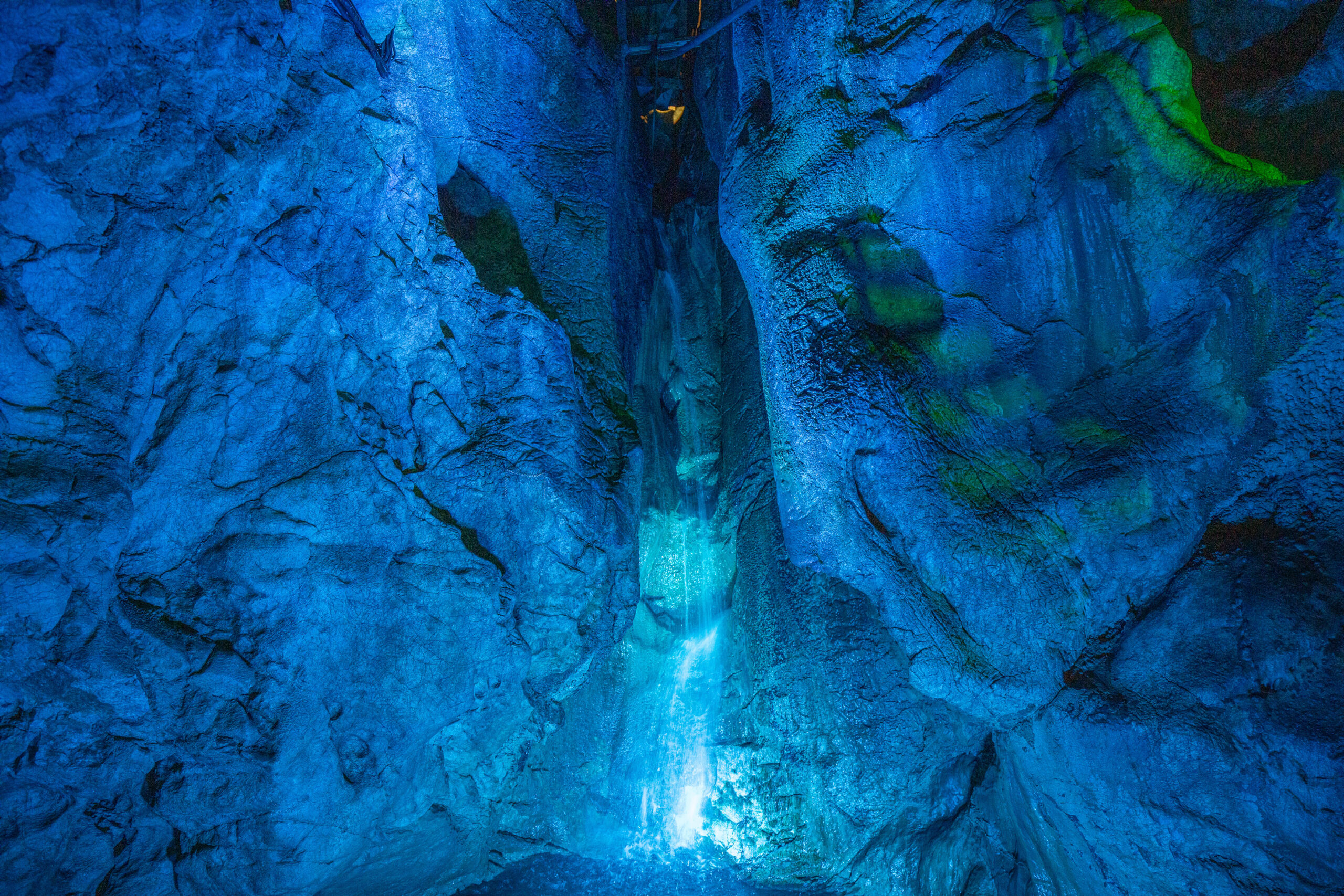 Blue-lit cavern walls with a bright light at the bottom center and a rocky, textured cave interior